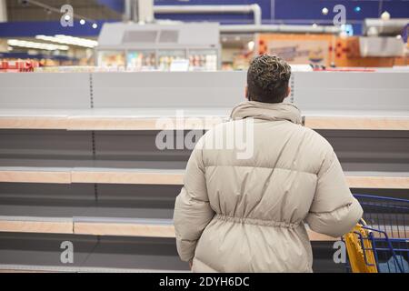 Rückansicht des Kunden mit dem Warenkorb, der leer aussieht Regale beim Einkaufen im Supermarkt Stockfoto