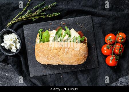 Sandwich mit frischem Camembert-Käse, Birnenmarmelade, Ricotta und Rucola. Schwarzer Hintergrund. Draufsicht Stockfoto