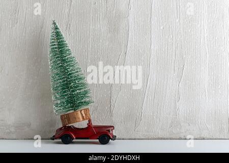 Künstlicher Weihnachtsbaum steht auf kleinem Spielzeugauto. Lieferung von Bäumen. Auto als Geschenk. Stockfoto