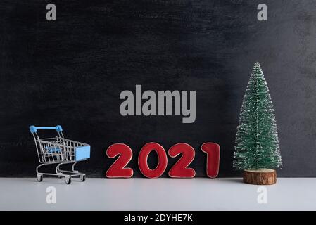 Miniatur-Weihnachtsbaum, Trolley-Wagen und Inschrift 2021 auf schwarzem Hintergrund. Shopping zum neuen Jahr. Stockfoto