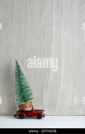Künstlicher Weihnachtsbaum steht auf kleinem Spielzeugauto. Lieferung von Bäumen. Auto als Geschenk. Speicherplatz kopieren. Stockfoto