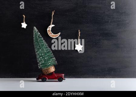 Kleiner Baum steht auf Modellauto auf schwarzem Hintergrund. Rund-um-die-Uhr-Lieferung für das neue Jahr. Stockfoto