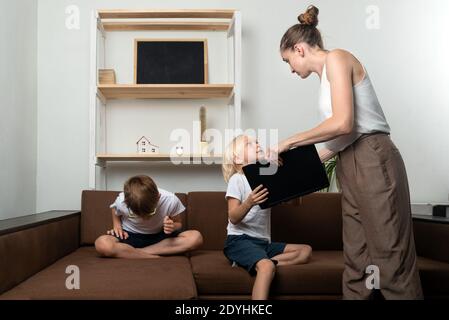 Mutter nahm den Kindern den Laptop weg. Mama mit Laptop in den Händen und zwei Jungen auf der Couch Stockfoto