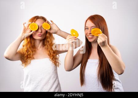 Zwei Mädchen haben Spaß und posieren mit orangen Scheiben. Skinimalismus und Spa-Konzept auf weißem Hintergrund Stockfoto