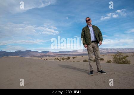 Ein aufstrebendes männliches Model zeigt seine Kleidung auf der Reise durch Badwater und Mesquite Sand Dunes im Death Valley National Park, Inyo County, USA Stockfoto