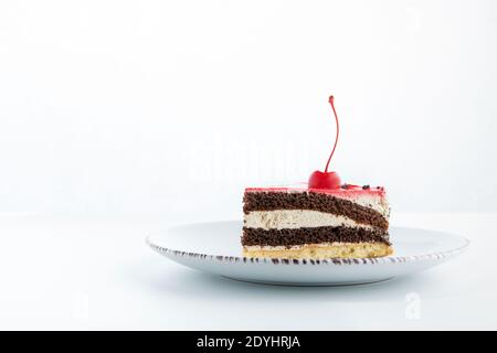 Schokolade und Vanillekuchen in Stücke geschnitten. Es gibt Kirsche oben. Seitenansicht zum Stück Kuchen auf weißem Hintergrund. Stockfoto