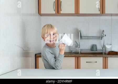 Blonde junge trinken aus großen Tasse in der Küche. Lustiges Schuljunge Frühstück. Stockfoto