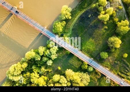 Luftaufnahme einer schmalen Straßenbrücke, die sich über einen schlammigen, breiten Fluss in grüner ländlicher Umgebung erstreckt. Stockfoto