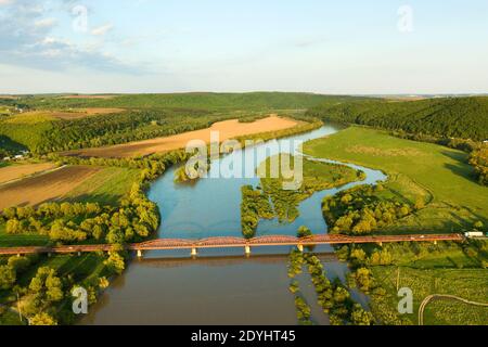 Luftaufnahme einer schmalen Straßenbrücke, die sich über einen schlammigen, breiten Fluss in grüner ländlicher Umgebung erstreckt. Stockfoto