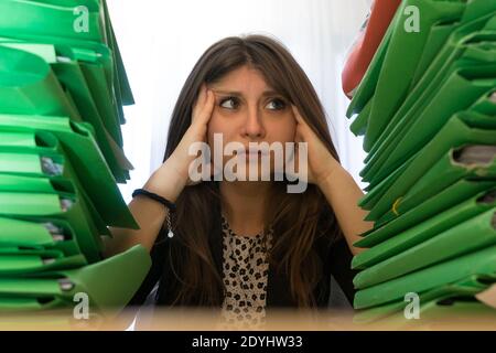 Büroangestellter betonte zwischen zwei massiven Stapeln von Aktenordnern zu kümmern. Stresskonzept der Mitarbeiter. Stockfoto