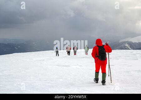 Rückansicht von Wanderern, die auf schneebedeckten Hügeln in Winterbergen wandern. Stockfoto