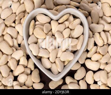 Große lima Bohnen in einem herzförmigen Schüssel Hintergrund und Textur. Draufsicht. Stockfoto