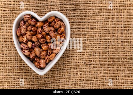 Weiße Cargamanto-Bohnen, auch als Cranberry, Borlotti oder Romano-Bohnen in einer herzförmigen Schale bekannt. Draufsicht. Stockfoto