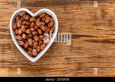 Weiße Cargamanto-Bohnen, auch als Cranberry, Borlotti oder Romano-Bohnen in einer herzförmigen Schale bekannt. Draufsicht. Stockfoto