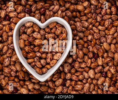 Weiße Cargamanto-Bohnen, auch als Cranberry, Borlotti oder Romano-Bohnen in einer herzförmigen Schale bekannt. Draufsicht. Stockfoto