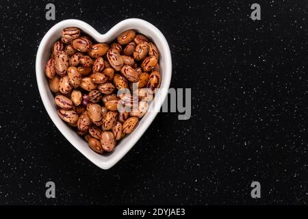 Weiße Cargamanto-Bohnen, auch als Cranberry, Borlotti oder Romano-Bohnen in einer herzförmigen Schale bekannt. Draufsicht. Stockfoto