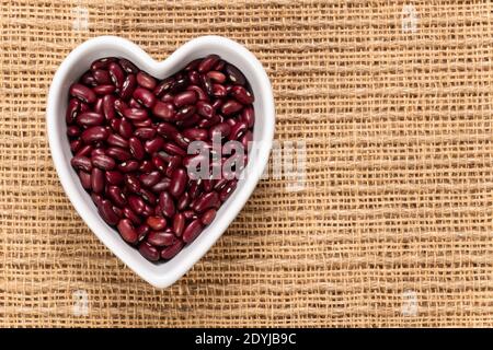 Korn von roten Bohnensamen in einer herzförmigen Schüssel Hintergrund und Textur. Draufsicht. Stockfoto
