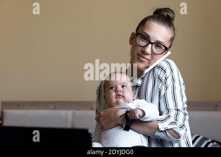 Kindheit, Mutterschaft, Familienkonzepte - erfolgreiche lächelnde reiche Geschäftsfrau Lady Mutter sitzen auf dem Bett mit Kleinkind Kind Baby sprechen am Telefon arbeiten Stockfoto