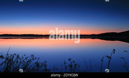 Der orange und blaue Himmel spiegelte sich auf dem friedlichen See Stockfoto