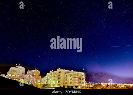 Fallender Stern oder ein Luftflugzeug, das in einem Sternenhimmel sichtbar ist Nacht über einem städtischen Wohnblock Stockfoto