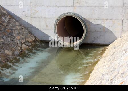 Großer Durchmesser Kunststoffrohr Sturmablauf Ablaufablauf mit abgedeckt Beton führt zu Abfluss Kanal mit Steinfliesen und umgeben Wasser auf kalt Stockfoto