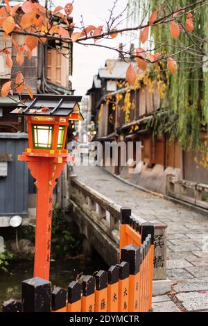 Kyoto Japan Rote, orange und gelbe Herbstblätter hängen über der traditionellen orangefarbenen Laterne in der Nähe des Tatsumi Daimyojin-Schreines in der Shinbashi Dori Street Stockfoto