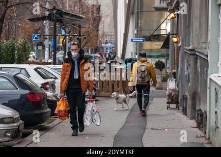 BELGRAD, SERBIEN - 29. NOVEMBER 2020: Mann mittleren Alters trägt eine Atemmaske und läuft in den Straßen von Belgrad mit einem Lebensmittelbeutel während c Stockfoto