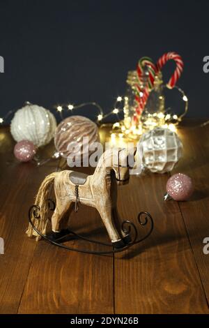 Weihnachtsdekoration - Holzspielzeug Schaukelpferd, Bälle für den Weihnachtsbaum, Silvester Süßigkeiten in einem Glas, umschlitzt mit einer glühenden Girlande auf einem Stockfoto