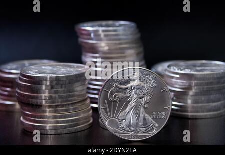Eine einzelne Silbermünze des amerikanischen Adlers, die aufrecht vor dem steht Stapel von American Eagle Dollar Silbermünzen Stockfoto