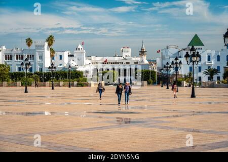 Tunis, Tunesien - Menschen, die entlang des Stadtplatzes mit dem Gebäude des Finanzministeriums im Hintergrund gehen Stockfoto