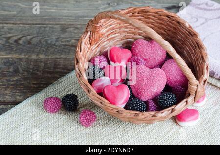 Kauartikel in Form von Herzen und Himbeeren in einem Korb, auf einem hölzernen Hintergrund. Selektiver Fokus Stockfoto