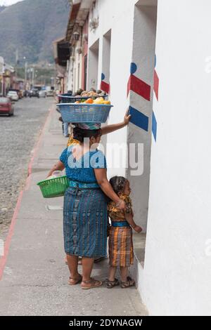 Antigua, Guatemala Frauen, die Obstkörbe auf dem Kopf tragen, posieren mit dem Mädchen Stockfoto