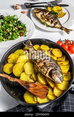 Abendessen mit gegrilltem Fisch aus der Meeresbrasse, Rucola-Salat mit Tomaten, gebackene Kartoffeln. Weißer Hintergrund. Draufsicht Stockfoto