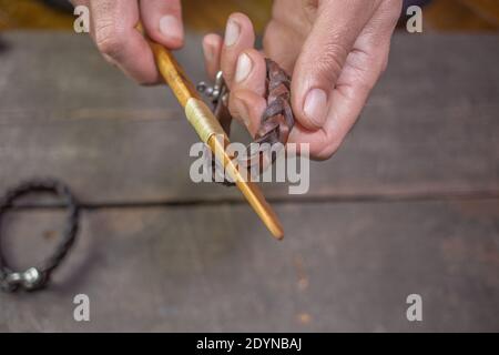 Armband Leder Handarbeit. Zopf-Zubehör. Man s Hände machen Handwerk Leder auf schönen Holz Hintergrund. Polierwerkzeug handgefertigt. Stockfoto