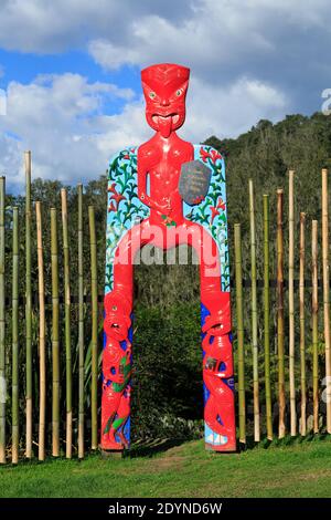 Ein farbenfrohes Holztor mit Maori-Schnitzereien menschlicher Figuren. Te Puna Quarry Park, Neuseeland Stockfoto