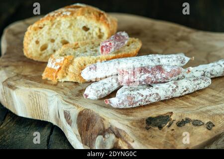 Kleine Finger spanischer Wurstffüße und Scheiben Weißbrot auf dem naturbelassenen Küchenbrett aus Holz auf dunklem Hintergrund. Gesunde Ernährung Konzept. Stockfoto