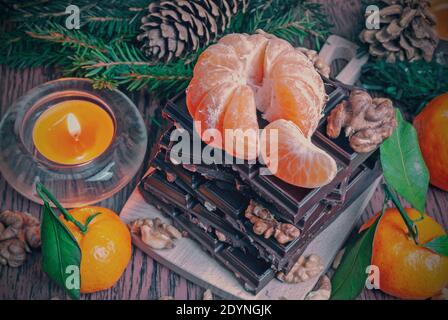Weihnachts- und Neujahrskomposition mit Mandarinen, Schokolade und Walnüssen auf dunklem Hintergrund Stockfoto