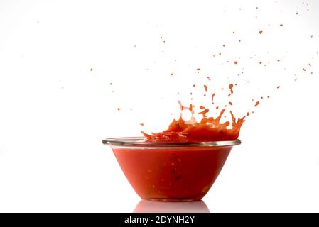 Tomatensauce spritzt aus Glasschüssel, isoliert auf weißem Hintergrund Stockfoto