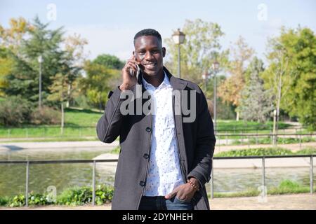 Junger afrikanischer schwarzer Mann, der auf dem Smartphone spricht und lächelt und die Kamera in einem Park anschaut. Geschäftsmann am Telefon. Stockfoto