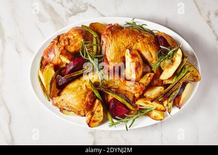 Geröstete Kartoffeln, Rote Bete, grüne Bohnen und Hühnerschenkel auf einem weißen ovalen Teller auf einem Marmortisch serviert, horizontale Ansicht von oben, flach liegend Stockfoto