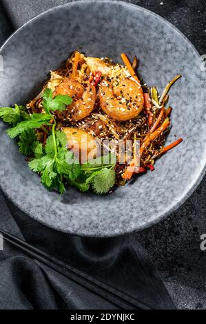 Reisnudeln unter Rühren mit Garnelen und Gemüse anbraten. Asien-Wok. Schwarzer Hintergrund. Draufsicht Stockfoto