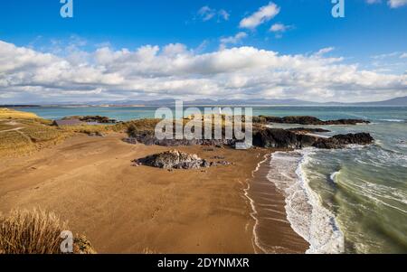 Ein Blick auf Twr Bach und die schneebedeckten Snowdonia Berge über Porth Twr Mawr auf Llanddwyn Island, Anglesey Stockfoto