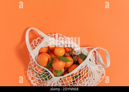 Mandarinen in Mesh-Einkaufstasche Draufsicht auf orangefarbenem Hintergrund. Zero Waste Shopping-Konzept. Stockfoto