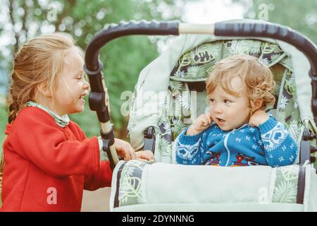 Schwester spielt mit ihrem Bruder im Kinderwagen, rollt das Baby die Straße hinunter Stockfoto