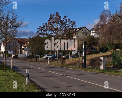 Moderne schwarz gefärbte Durchzugskamera für Geschwindigkeitskontrolle am östlichen Ortseingang mit Fußweg, Straße und Wohngebäuden. Stockfoto