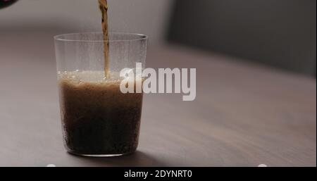 Gießen Sie Cola in Glas mit Eis auf Walnusstisch mit Kopierraum, breites Foto Stockfoto