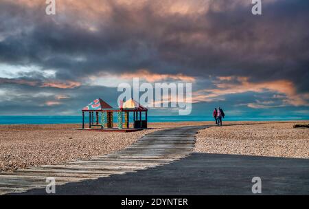 Ein Paar, das an Kunstwerken von Sol Calero, Folkestone Beach, Folkestone, Kent, England vorbeiläuft Stockfoto