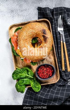 Bagel-Sandwich mit Lachs, Frischkäse, Spinat und Ei auf einem Holzteller. Grauer Hintergrund. Draufsicht Stockfoto