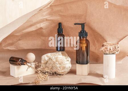 Braune Glasflaschen von Kosmetikprodukten auf Stein, geometrische Holzformen und getrocknete Blumen auf beigem Papierhintergrund. Natürliches organisches Spa Kosmetik B Stockfoto