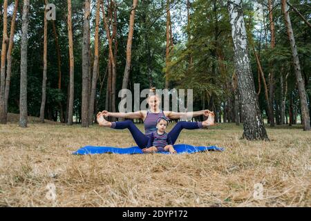 Sicheres Fitnessstudio oder Fitnesscenter im Freien. Familie durch gemeinsames Training in Parks fit bleiben. Mutter praktiziert Yoga mit ihrem Baby Tottdler Tochter in der Stockfoto